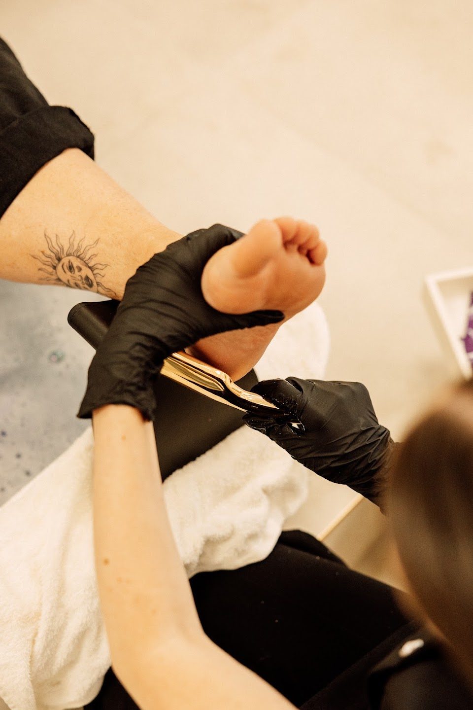A therapist in black gloves treating a client's foot during a pedicure